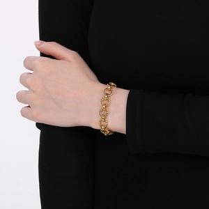 Détail d'un bracelet gourmette en acier titane doré porté sur une manche noire polie
