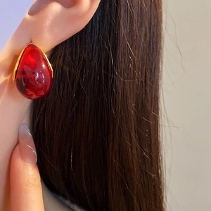Close-up of a red teardrop resin earring with gold trim worn by a female model