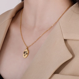 Close-up of a gold oval floral pendant necklace worn over a beige blazer for a chic look