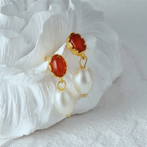 Detailed close-up of retro gold earrings with red agate and water-drop pearls
