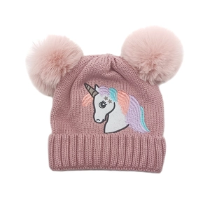 Détail du bonnet en tricot rose avec broderie licorne et deux pompons en fausse fourrure