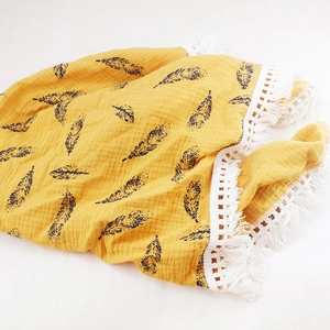 Close-up of ginger muslin baby blanket with black feathers, lace edges and tassels