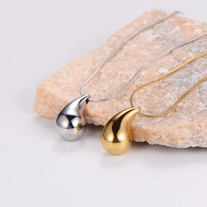Close-up of polished gold and silver teardrop pendants on stone with snake chains