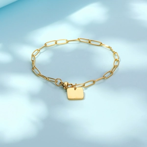 Elegant gold paperclip chain bracelet featuring a polished square pendant on blue background