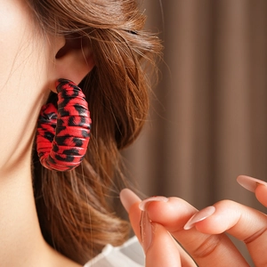 Close-up of red and black leopard print woven C-shaped earrings on a model's ear