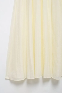Detailed macro view of the light yellow pleated skirt showing texture and fabric craftsmanship