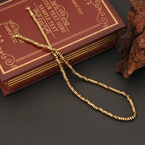 Dettaglio di una collana di perle sfaccettate dorate con chiusura a moschettone e catenina