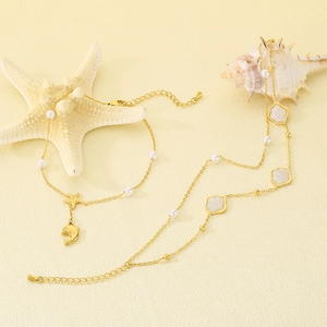 Detalle de conjunto de tobilleras doradas de tema marino con delfín, estrella y perlas.