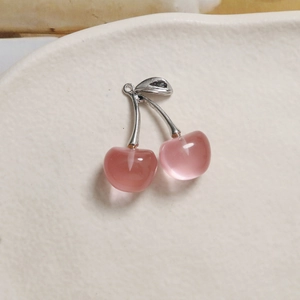 Macro detail of translucent pink cherry charms with silver metal stems and green leaves