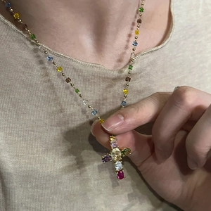 Gros plan d'un collier croix doré avec zircons colorés porté par une femme