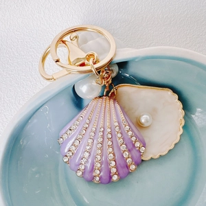 Close-up of a luxury purple enamel seashell keychain with sparkling rhinestones and pearls
