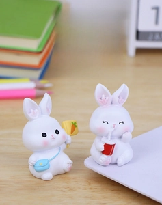 Close-up of two cute resin rabbits with carrot sign and red cup on a wooden desk