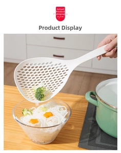 White long-handle strainer scooping noodles and broccoli from a glass bowl