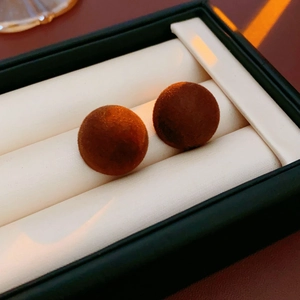 Macro shot of dark brown flocked spherical stud earrings resting in a black jewelry box