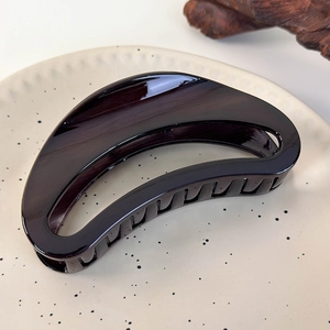 Detailed close-up of dark tortoiseshell hollow crescent hair claw clip on ceramic dish