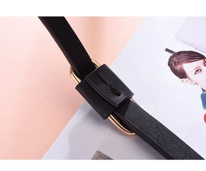 Detail of slim black leather belt featuring a golden double ring buckle on a fashion magazine