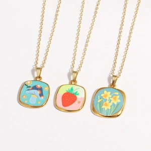 Close-up of gold necklaces featuring mushroom, strawberry, and flower enamel pendants