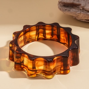 Dettaglio di un bracciale ondulato in resina ambrata con trama tartarugata lucida