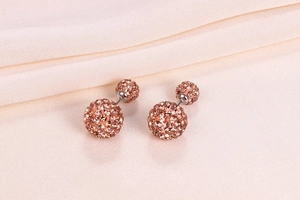 Detail of rose gold Shamballa stud earrings with double crystal balls on pink fabric