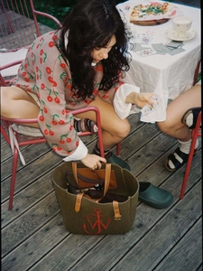 Olive green felt tote bag with leather handles and red anchor logo on wooden deck