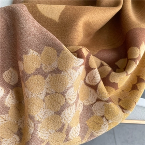 Detailed macro view of the knitted leaf pattern and thick texture of the brown scarf