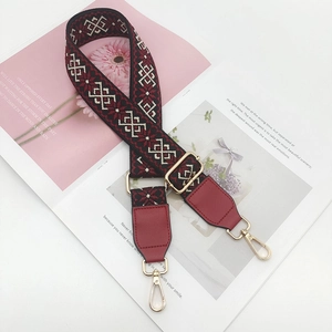 Close-up of geometric jacquard bag strap with red leather ends and gold-tone swivel hooks