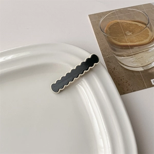 Detail view of the glossy black wave-shaped hair clip with white edge on a ceramic plate