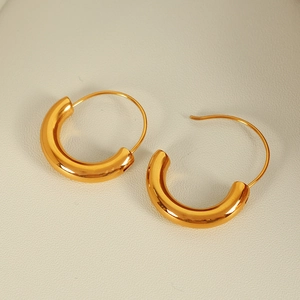 Polished 18K gold plated C-shaped chunky hoop earrings on a beige leather texture background