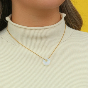Close-up of a delicate gold chain necklace with a round white opal stone on a model