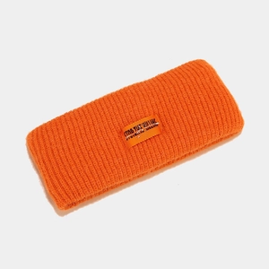 Detail of a bright orange ribbed knit headband featuring a central woven logo label