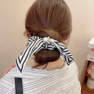 Close-up of a striped bow scrunchie with a large pearl and diamonds on a high bun