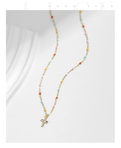 Close-up of golden cross necklace with colorful beads and zircon on white background