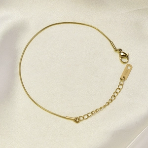 Macro detail of 18K rose gold snake chain anklet with lobster clasp on beige silk