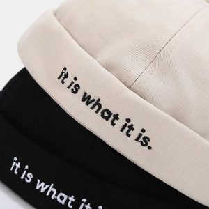 Detail of embroidered 'it is what it is' text on beige and black miki hats