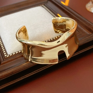 Dettaglio di bracciale rigido dorato irregolare con tacca geometrica su legno