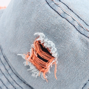 Dettaglio del cappello in denim azzurro lavato con strappo e cuciture arancioni a contrasto