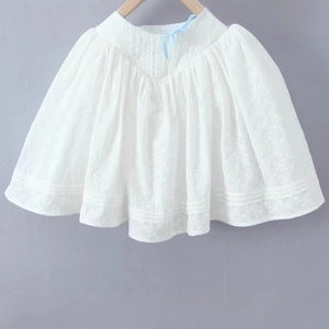 Elegantes weißes besticktes Kinderkleid mit blauen Banddetails hängend an einem Holzbügel