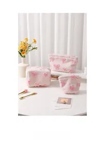 Three-piece set of pink plush makeup bags with embossed bow patterns on a table