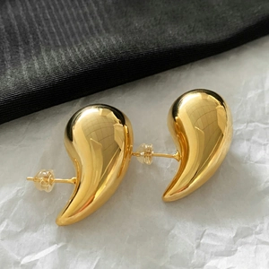 Detailed macro view of high-polished golden bean stud earrings on a textured background