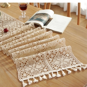 Detail of handmade crochet table runner with beige lace floral hollow out patterns and tassels
