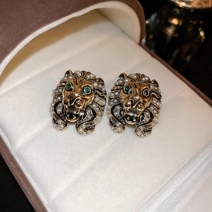Detailed view of gold lion head earrings with green eyes and white pearls in a jewelry box