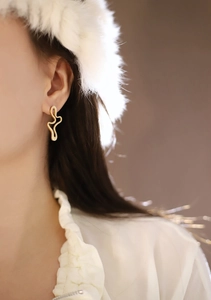 Close-up of golden irregular wavy earrings on model featuring polished metallic texture