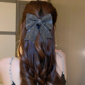 Close-up of a sparkling black bow hair clip with rhinestones on long brown wavy hair