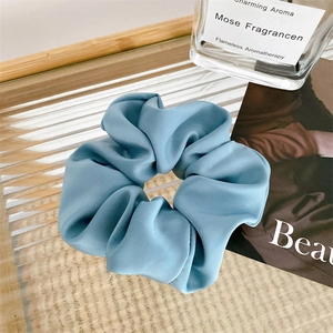 Detail of misty blue satin scrunchie on a glass tray with premium aesthetic styling