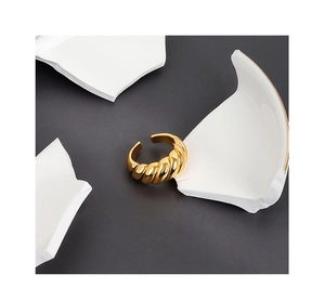 Detail of a golden twisted croissant ring with metallic texture on a minimalist dark background