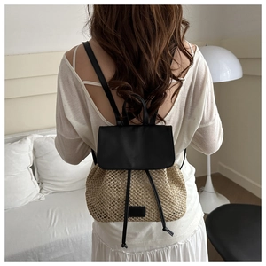 Rear view of a model wearing the woven straw backpack with black leather flap detail