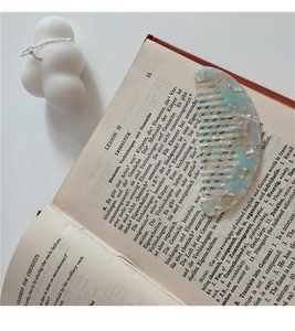 Close-up of a marble acetate wide-tooth comb on an open book with minimalist styling