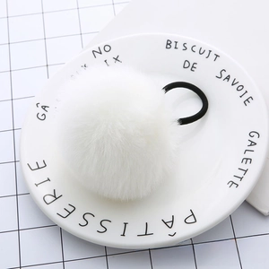 Close-up of a white fluffy faux fur pom pom hair tie on a white porcelain plate