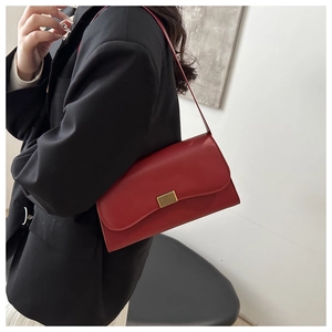 Detail view of a stylish red shoulder bag with gold hardware worn with a black blazer