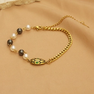 Detail of golden Cuban chain bracelet with pearls, black beads and green enamel pendant